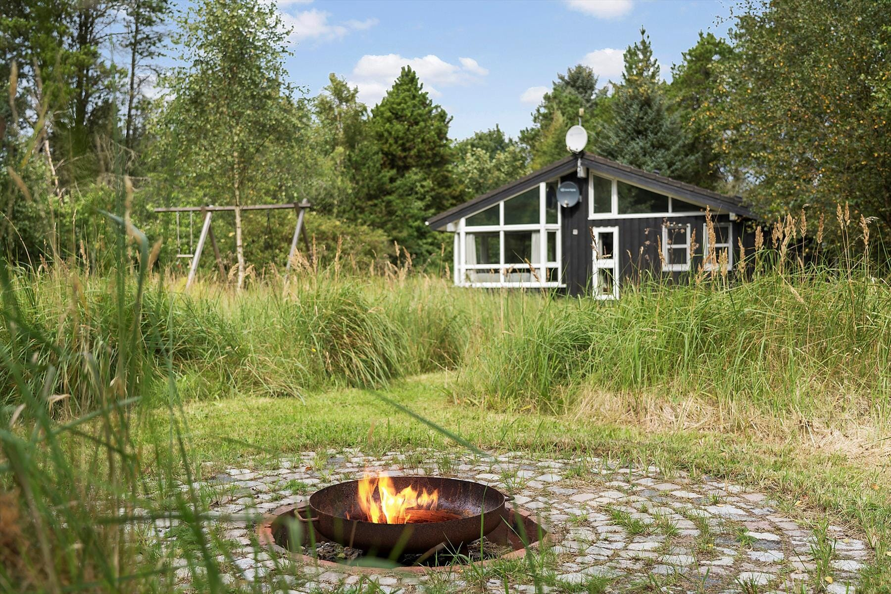Sommerhus på Bredvandet 34 i Svinkløv set udefra på en sommerdag med ild i bålstedet
