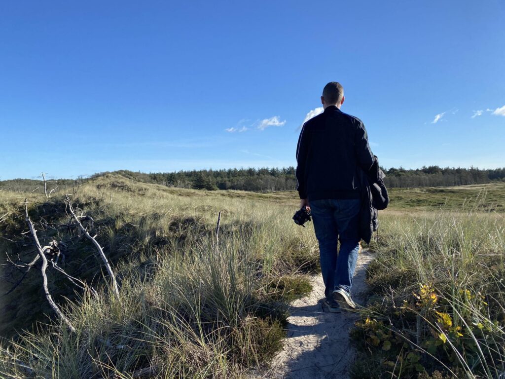 Mand går på strandsti under blåhimmel