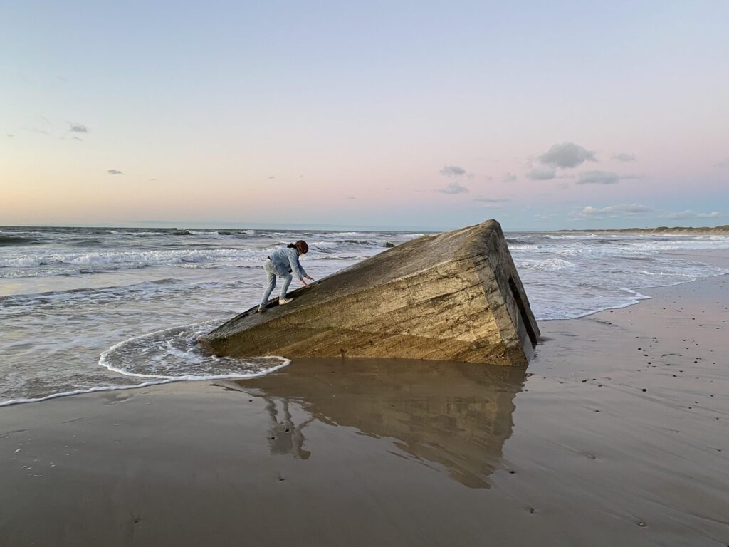 En pige klatrer op ad en bunker i vandkanten på stranden