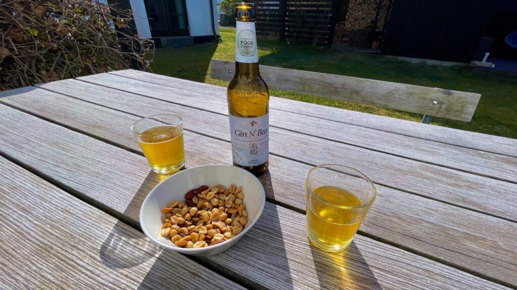 To glas Gin & Beer fra Thisted Bryghus og en skål med blandede nødder på et havebord