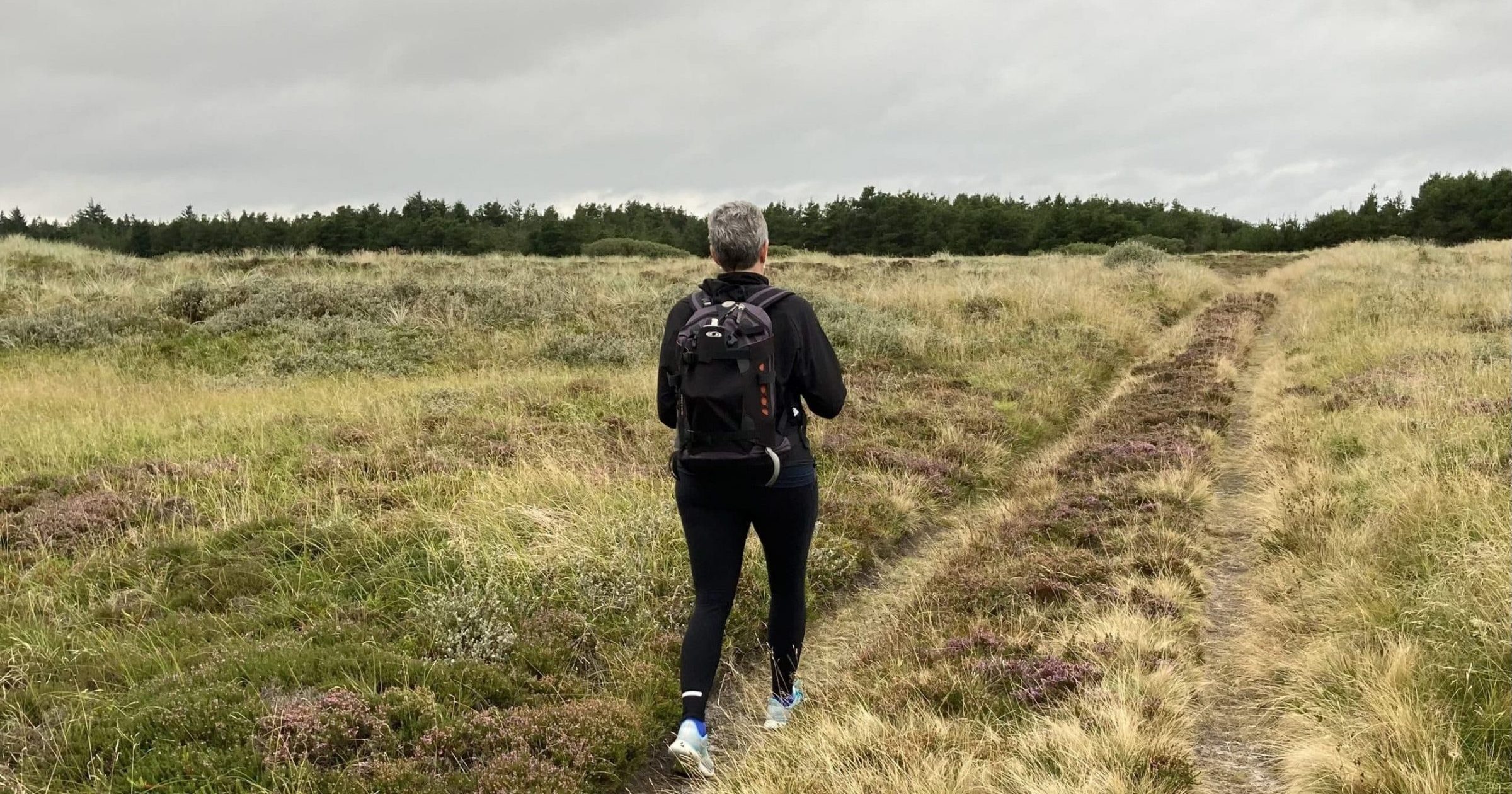 Kvinde vandre på en sti mellem græs og lyng