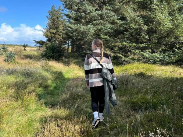 Kvinde går med raske skridt gennem Lodbjerg Klitplantage på en solskinsdag