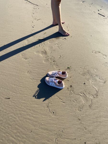 Lyserøde Adidas sneakers står i sandet på stranden