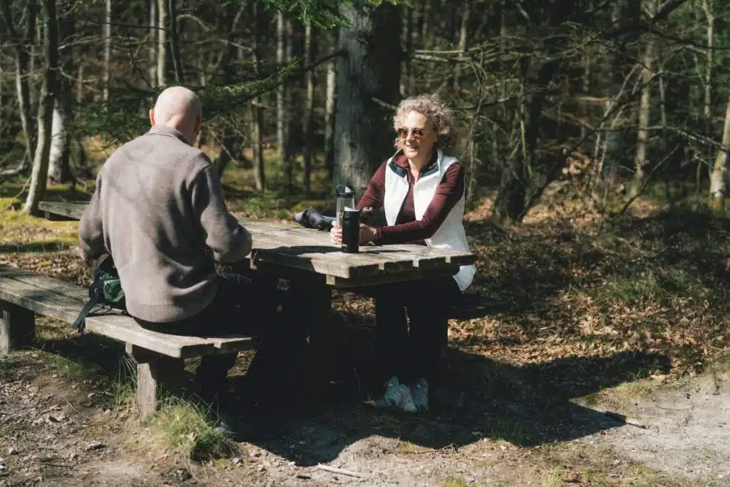 Par sidder ved en bænk i skoven og er ved at finde deres madpakker frem