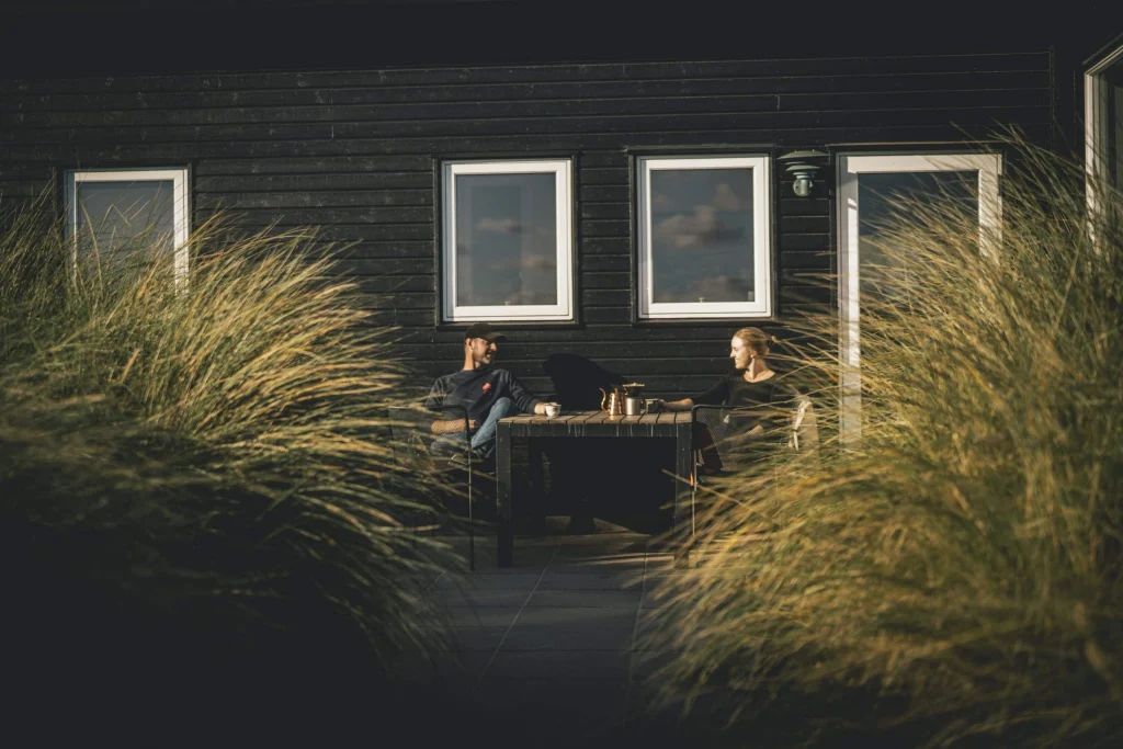 Par sidder ved et havesæt udenfor sommerhus med en kop kaffe og snakker