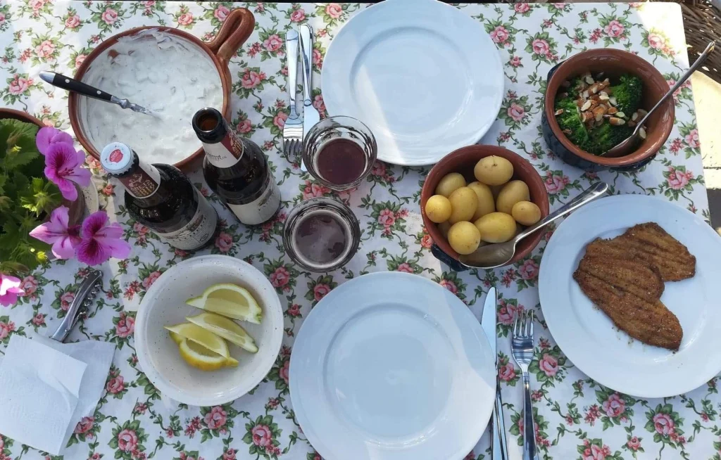 Havebordet med blomstret dug anrettet med kartofler stegt fisk og salat