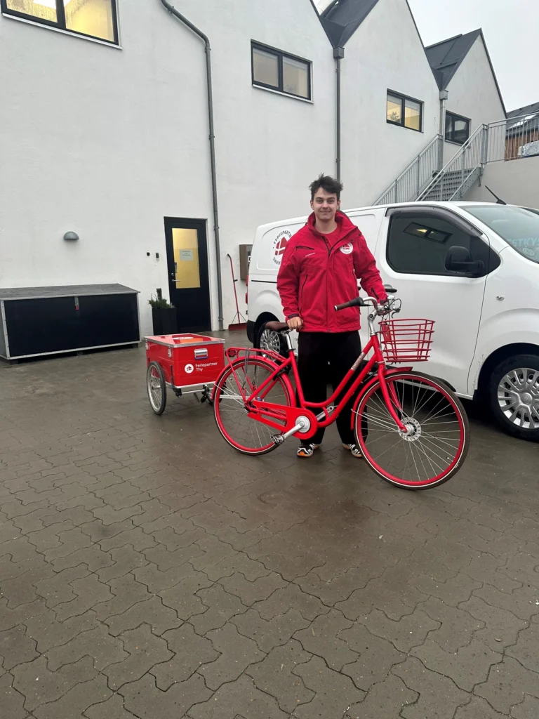Ung mand står med en rød cykel med en rød cykeltrailer med Feriepartner logo