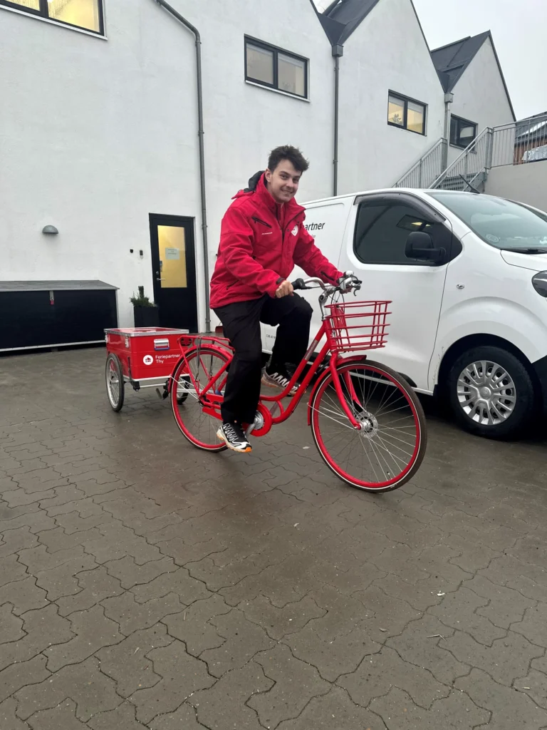 Ung mand cykler på en rød cykel med en rød cykeltrailer med Feriepartner logo