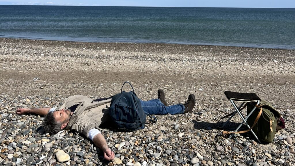 Mand ligger ved stranden og lytter til havets brusen Gåture som modvægt til stress i naturen